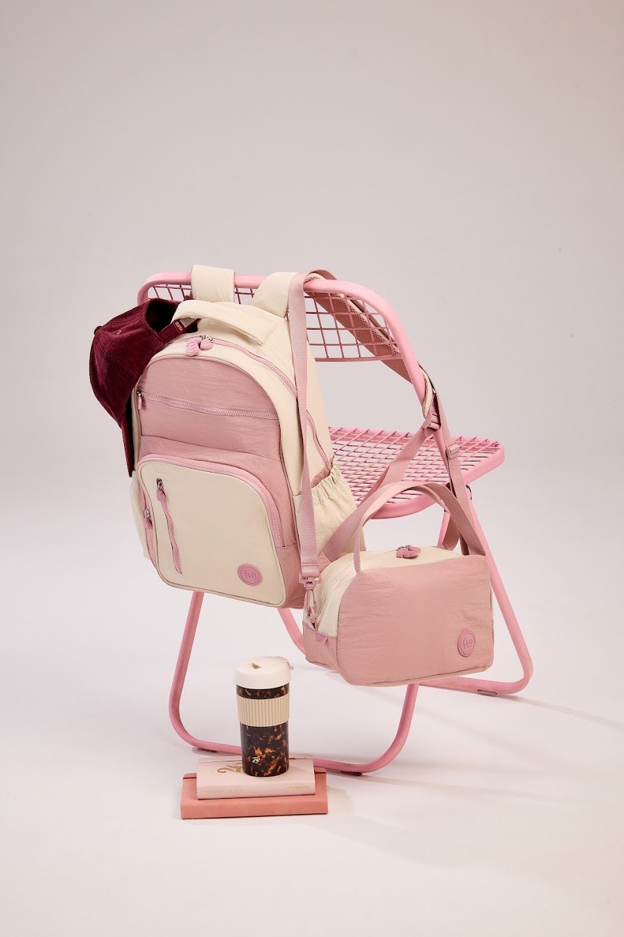 Mochila y cartuchera FW en tonos rosas sobre una silla plegable, junto a un vaso térmico