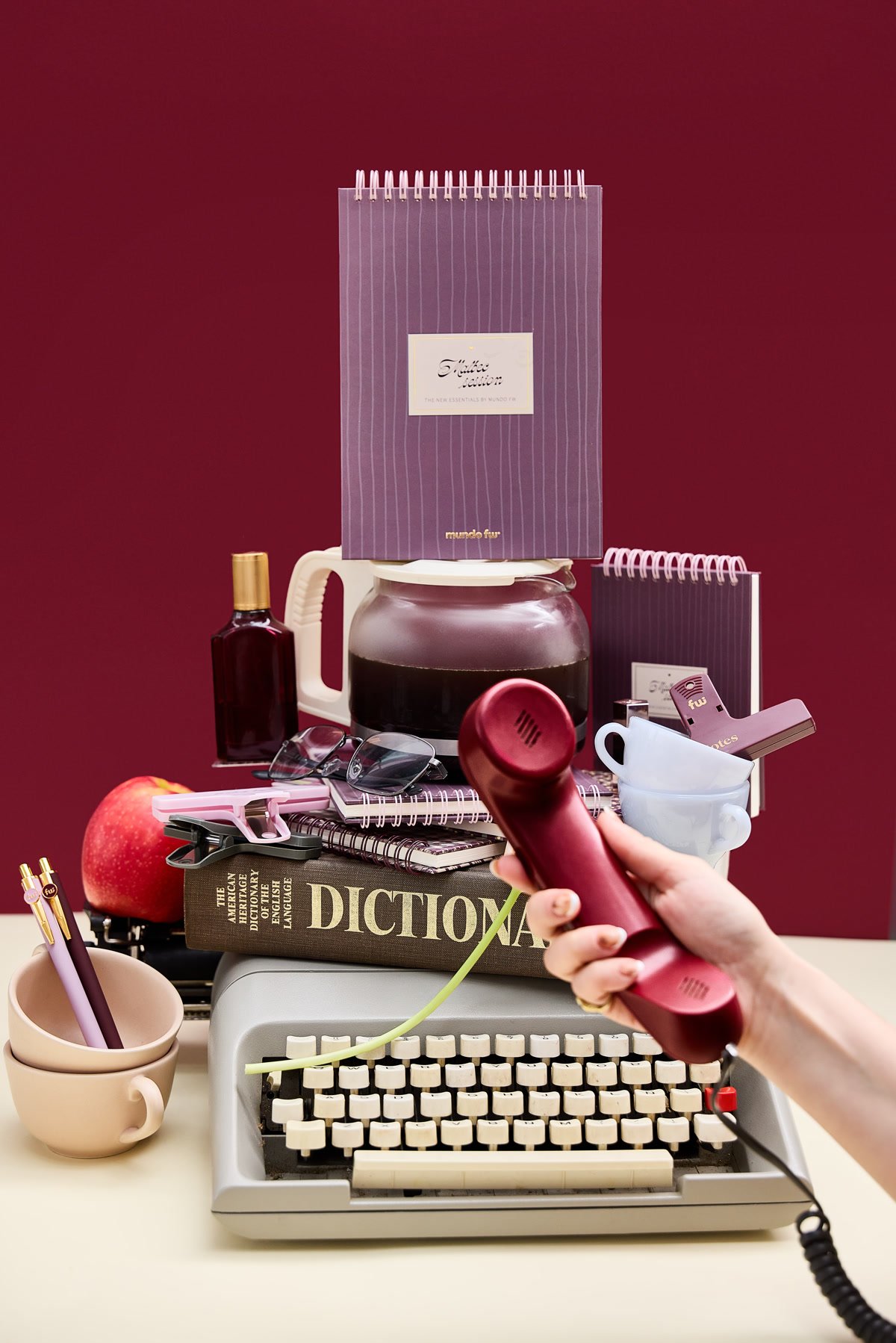 Cuadernos FW en tonos borgoña, una máquina de escribir y un teléfono retro sobre un escritorio
