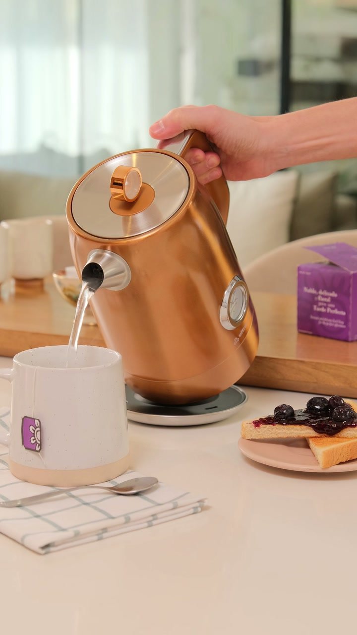 Una mano sirve agua desde una pava eléctrica cobriza Ultracomb hacia una taza, junto a tostadas